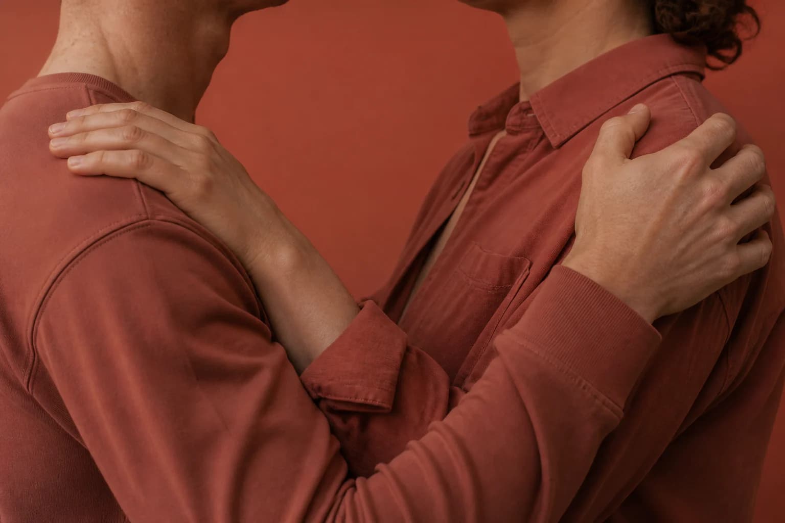 Twee mensen in terracotta kleding leggen hun handen op elkaars schouders